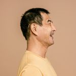 Side profile of a smiling senior man in a casual outfit against a brown background.